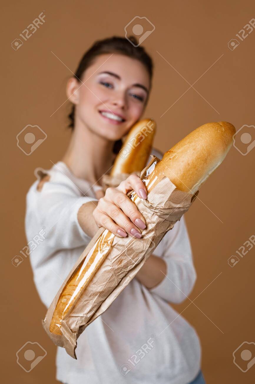 866x1300  Красивая улыбающаяся молодая женщина, держащая хлеб в бумажном пакете на студийном желтом фоне. Девушка показывает свежий ароматный длинную буханку. Сосредоточьтесь на хлебе Стоковое фото, изображение и изображение без роялти. Изображение 141336399.