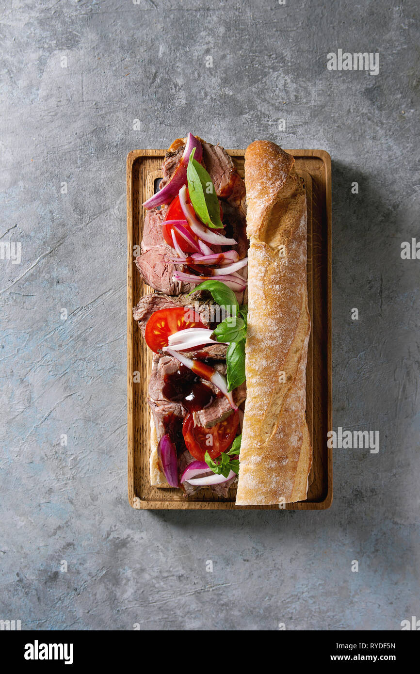 866x1390  Сэндвич с говядиной багет с помидорами, базиликом, красным луком, подаваемым на деревянной порции на сером фоне текстуры. Плоская летала, пространство Стоковое фото - Alamy