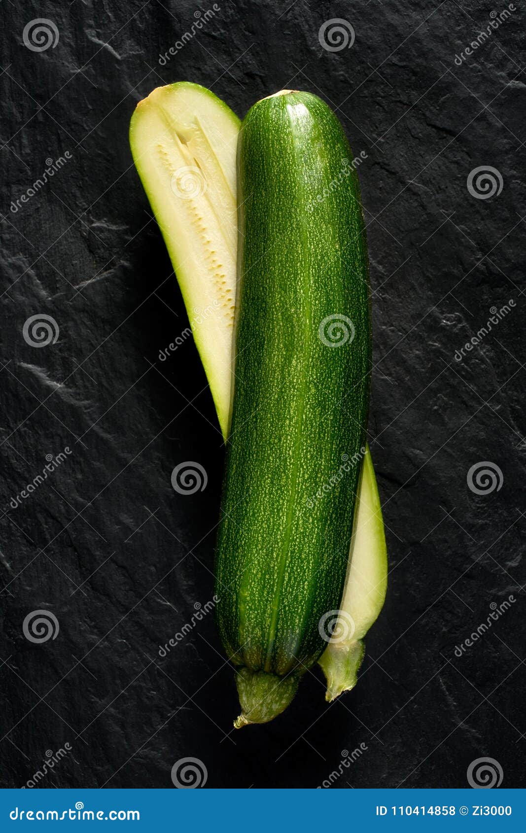 1067x1690  Зеленый цуккини вырезан пополам на черном фоне.