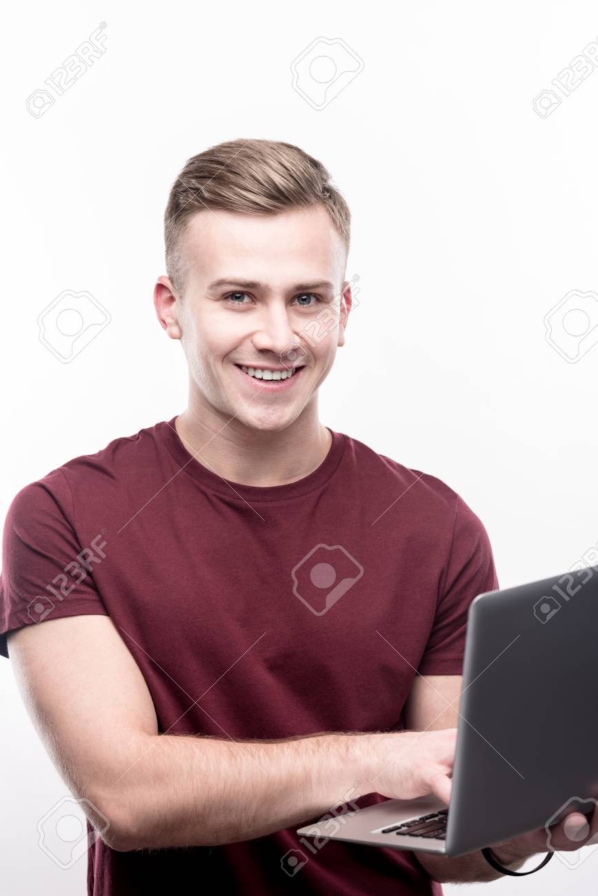 867x1300  Лучший это специалист. Красивый светловолосый молодой человек в бордовой футболке, работающий над его ИТ-проектом и позирует для камеры, когда он изолирован на белом фоне Stock Photo, Picture и
