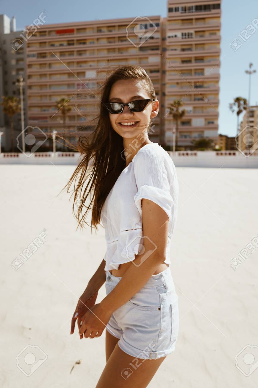 867x1300  Модная загорелая девушка позирует на пляже, глядя на камеру. Испанские пляжи Стоковое фото, картинки и роялти изображение. Изображение 121142540.